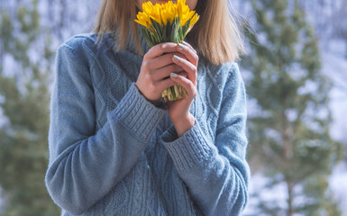 woman with a yellow bouquet of spring flowers in her hands on a snow day