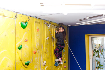 little girl climbing a rock wall indoor.