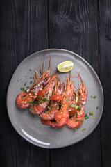 Langoustines cooked in garlic sauce on a grey plate on a dark wooden background, top view.