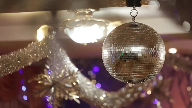 Silver Mirror Disco ball with bright rays, party with blurred background. Rotating disco mirror ball