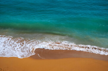 Obraz premium Aerial view of surf in turquoise sea meets red sandy beach