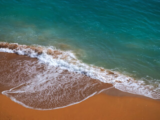 Aerial view of surf in turquoise sea meets red sandy beach