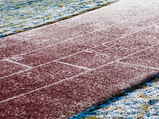Fototapeta premium Running track partially covered with ice and snow. Dangerous surface conditions in winter cold season. Nobody. Sport training area.