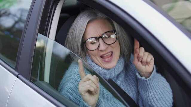 Happy senior woman dancing and singing sitting in car, good news in the morning
