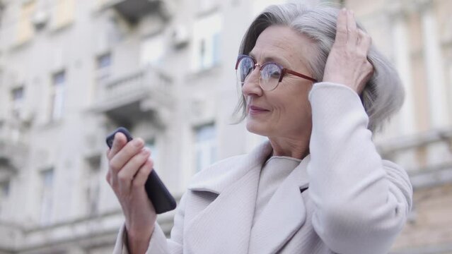 Elegant mature woman with stylish hairdo texting on smartphone, waiting for man