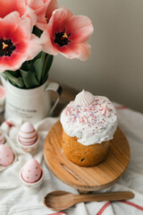 Easter symbols colored eggs and Panettone. Easter cake and decorated served wood table. Pink tulips in a metal jug.