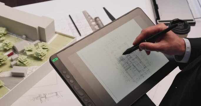 Man architect uses tablet computer and draws project of building