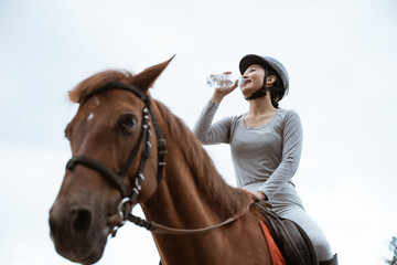Equestrian athlete on horse while drinking with bottle on white sky background