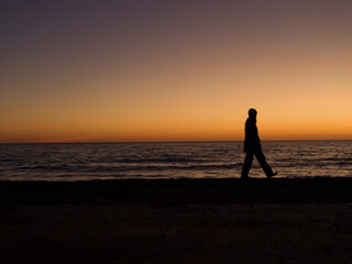 silhouette of person walking on the beach at sunset