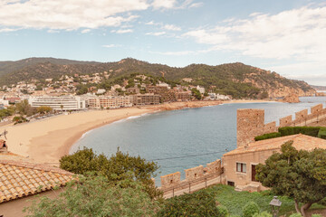 Panorámica de la playa de Tossa del Mar desde el Castillo Vila Vella con las barquitas estacionadas en la arena y las casa del pueblo al fondo delante de la verde montaña.