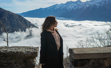 Girl posing next to the fence, with beautiful background with a fog revealing mountain, Ligurian Alps, Piedmont region, Province of Cuneo, north-western Italy
