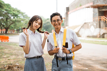 Geeky boy student in glasses smiling with girl friends in uniform on outdoor background