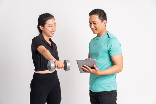 sporty woman lifting dumbbells and man guiding while using a pad on isolated background