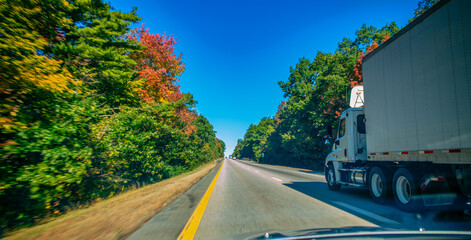 American style truck on freeway pulling load. Transportation theme. Giant truck along New England...