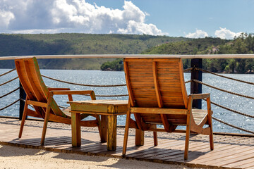 Two empty chairs and small wooden table facing view with beautiful lake and mountains