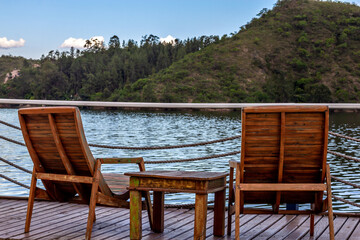 Two empty chairs and small wooden table facing view with beautiful lake and mountains