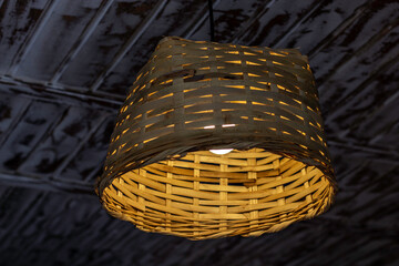 Lit light fixture made of wicker on white painted rustic wooden ceiling