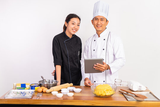 two chefs smiling while holding tablets and preparing cooking ingredients on table on isolated background