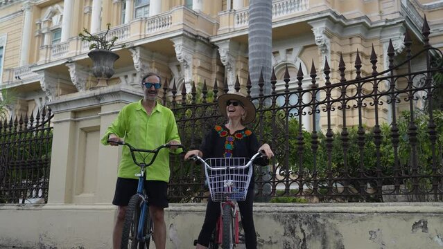Attractive, mature elderly retired man and woman in ethnic clothing laughing together on bikes on the Montejo Central Avenue with museums, restaurants, mansions in Merida, Yucatan, Mexico.