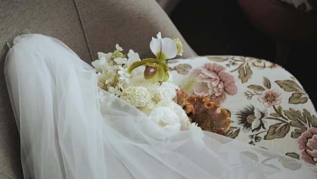 The bride's white veil and beige color bouquet on a chair, wedding accessories, slow motion shot.