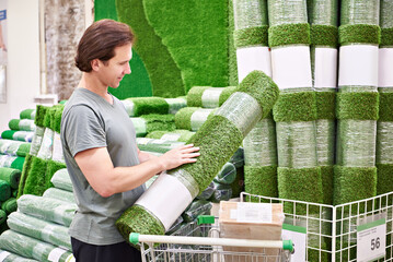 Man buying rolls of artificial grass turf in store