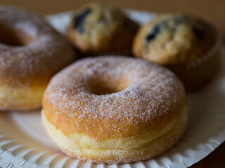 Sugar donut on white paper plate with other cakes.