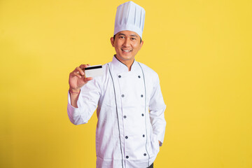 asian male chef wearing chef jacket showing credit card standing on isolated background