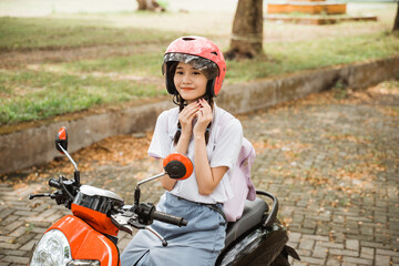 Asian student girl smiling while tightening helmet strap on motorbike