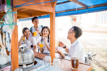 group of asian high school students in uniform chatting while enjoying a drink at an angkringan