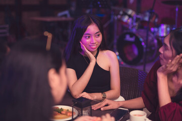 A good-looking Asian lady rests her face on her palm as she attentively listens to her friend gossiping about a recent issue. Friends catching up with each other while eating out in a restaurant.