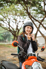 Fototapeta na wymiar Attractive student girl wearing helmet strap while riding motorbike to school