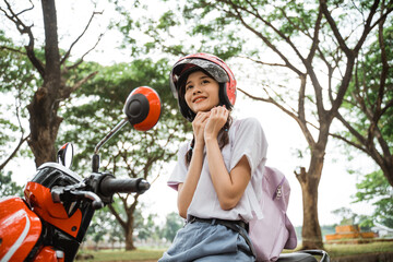 Student girl carrying school bag tightens helmet strap while going to ride on motorbike