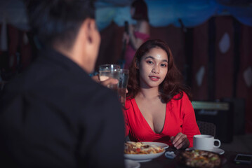 Asian couple makes toast to their romantic relationship as they celebrate valentine's day by having a dinner date at an indoor restaurant with live band.