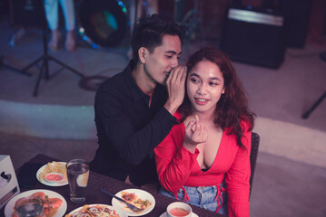 The boyfriend whispers to the girlfriend's ear as he shares a dirty secret. Asian man telling a woman a sexy inside joke.