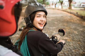 Student girl wearing helmet and jacket looking back to ask a question while riding a motorcycle together
