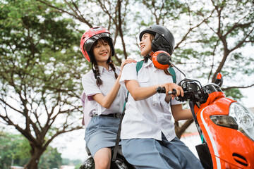 Naklejka premium Two girls in high school uniforms wearing helmets chatting while riding a motorcycle together