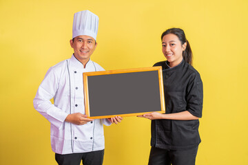 male chef with female chef showing a blank blackboard on isolated background