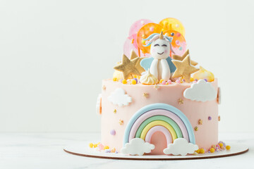 Unicorn cake with pink cream cheese frosting decorated with mastic rainbow, multicolored caramel candies and unicorn shaped figure on top. Birthday cake for a little girl on the white background © alexanderon