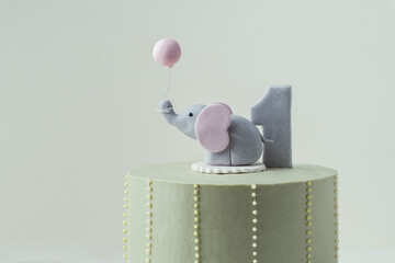 Birthday cake for a one year old baby. Baby shower party cake. Birthday cake for a little kid with pastel green frosting decorated with elephant shaped mastic figure on the grey background.