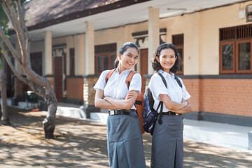 Two high school teenagers standing back to back with crossed arms in the schoolyard