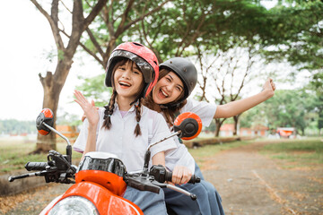Obraz premium Two student girls wearing helmets waving while riding motorbikes on the street