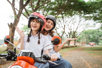 Naklejka premium Two student girls wearing helmets smiling for the camera while riding motorbikes on the street