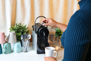 Closeup female hand insert espresso coffee capsule into automatic espresso machine to make fresh...