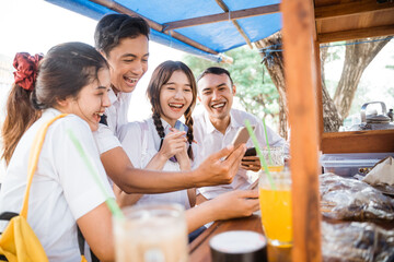 Four high school kids using smartphones together while joking in a shop