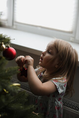 Little girl decorating christmas tree with toys and baubles. Cute kid preparing home for xmas celebration.