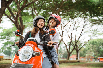 Fototapeta na wymiar Two high school student girls wearing helmets and jackets enjoying a motorcycle ride together