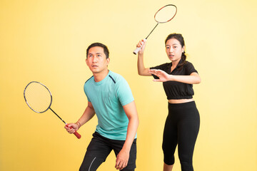 asian man and woman holding racket in ready position for shuttle on yellow background