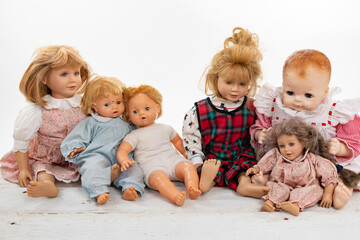 Fototapeta na wymiar Collection of multiple dolls sitting on a rough white wooden table isolated on white with copy space