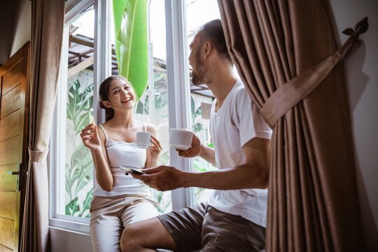 young couple chatting while enjoying a cup of coffee while using a tablet sitting at the window