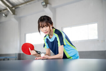 Close up of a female athlete holding a paddle and a ball ready to serve in a ping pong match - obrazy, fototapety, plakaty